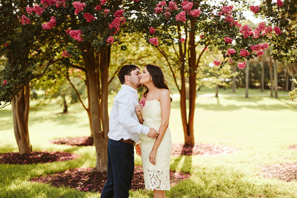 engaged couple kissing under a tree of white flowers