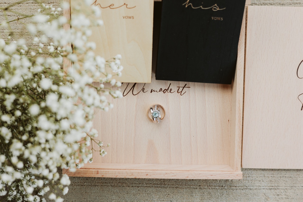 wedding rings on a box with flowers and vow books near it